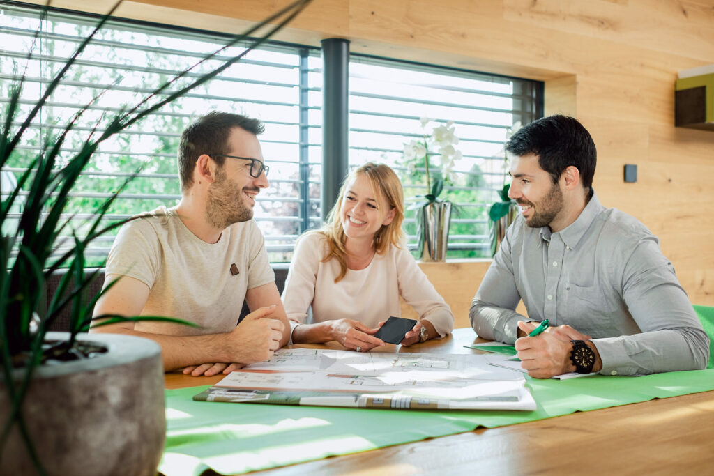 Beratungsgespräch am Tisch: drei Personen besprechen einen ausgedruckten Hausplan